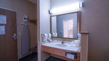 A hotel bathroom with a wooden vanity, a large mirror, and a shower area.