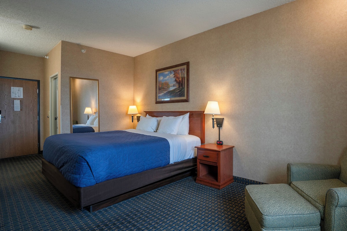 Een hotelkamer met een groot bed, twee bedlampen, een nachtkastje, een stoel en een schilderij aan de muur.