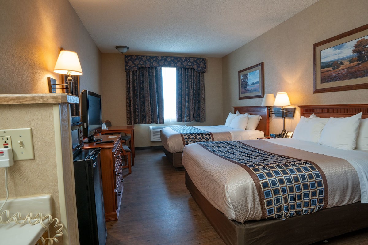 Een hotelkamer met twee bedden, een bureau met televisie, een raam met gordijnen, en een schilderij aan de muur.