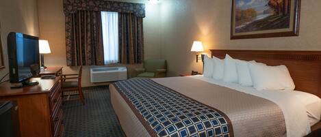 A hotel room with a large bed, a desk with a television, a chair, and a painting on the wall.