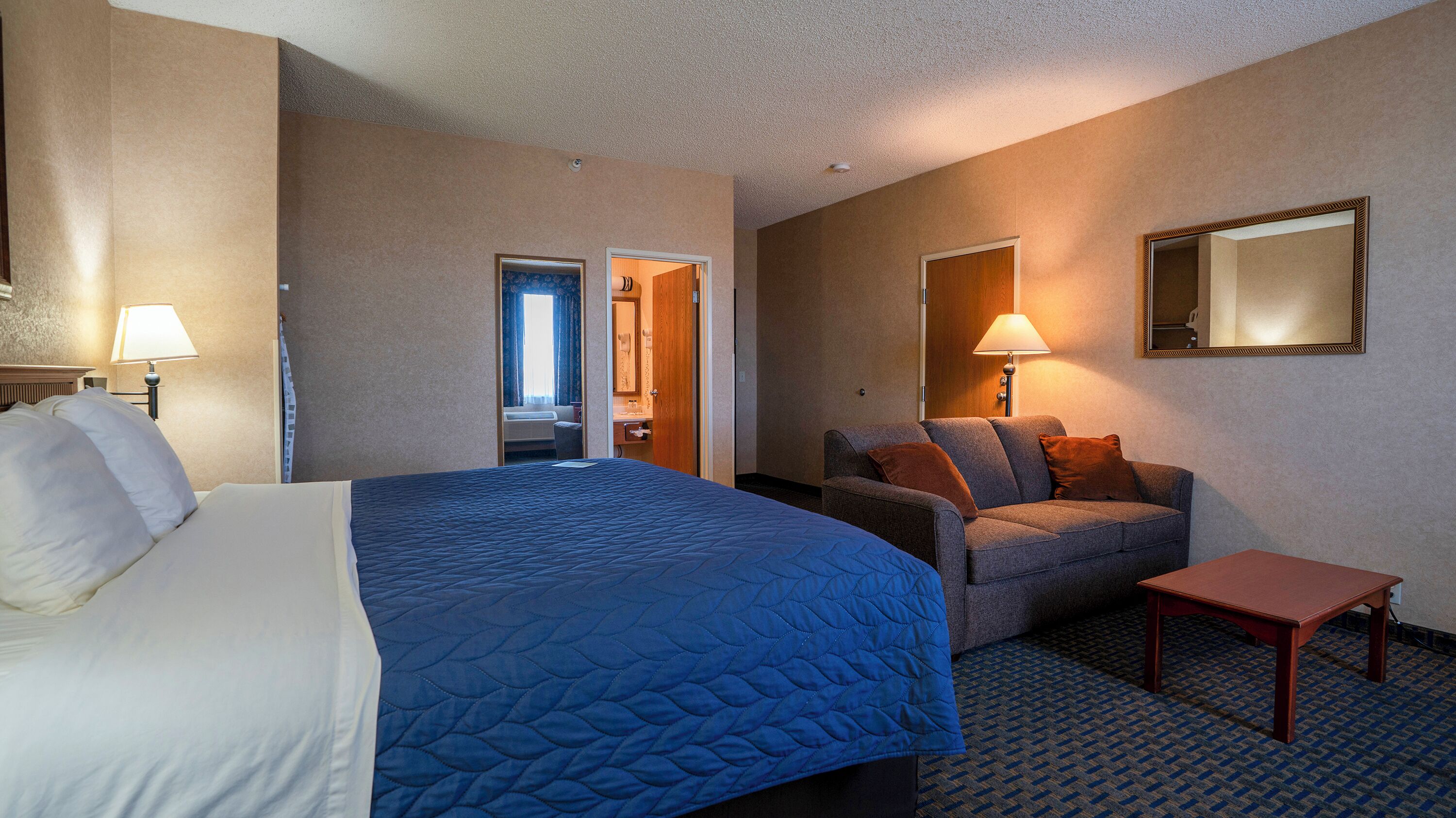 A hotel room with a large bed, a sofa, a small table, and a mirror on the wall.
