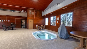 Un intérieur en bois avec une piscine, une table couverte et une porte donnant sur une autre pièce.