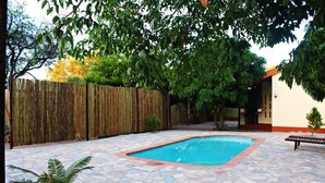 Un patio trasero con piscina, suelo de piedra, cerca de madera y un banco.