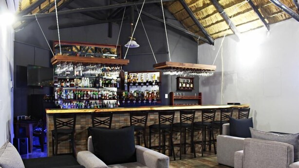 Zona de bar con mostrador de madera, varios taburetes y un área de estar con sofás y sillones.