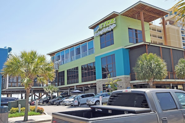 A multi-story building with a green and blue facade, large windows, and a parking lot with several cars.