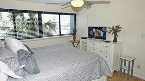 A bedroom with a bed, a television, a dresser, a small table, and a ceiling fan. - 3BR Condo in Myrtle Beach: Perfect for Families (MYRTLE BEACH)