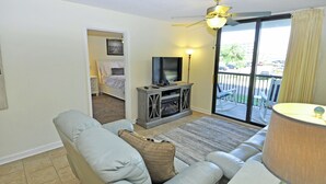 A living room with a sofa, a television on a stand, a ceiling fan, and a view through a sliding glass door to the outside. - 3BR Condo in Myrtle Beach: Perfect for Families (MYRTLE BEACH)