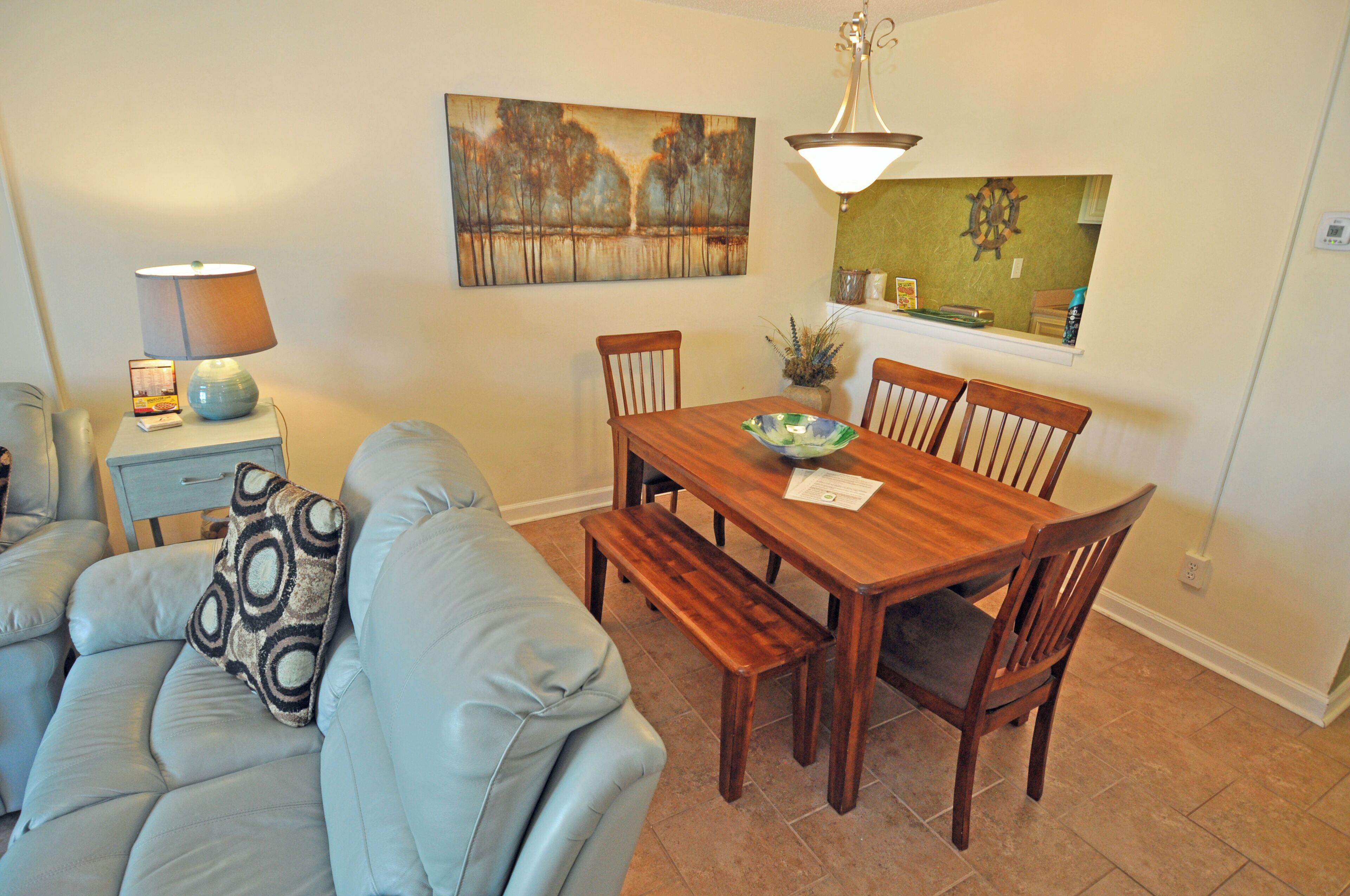 A dining area with a wooden table, chairs, a bench, a lamp, a painting, and a small plant on a shelf.