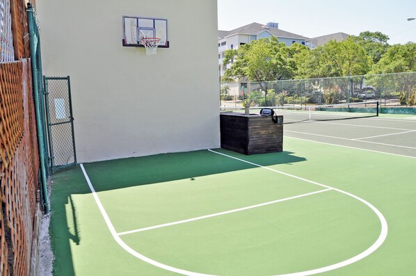An outdoor tennis court with a basketball hoop, a wooden bench, and a chain-link fence. - 3BR Condo in Myrtle Beach: Perfect for Families (MYRTLE BEACH)