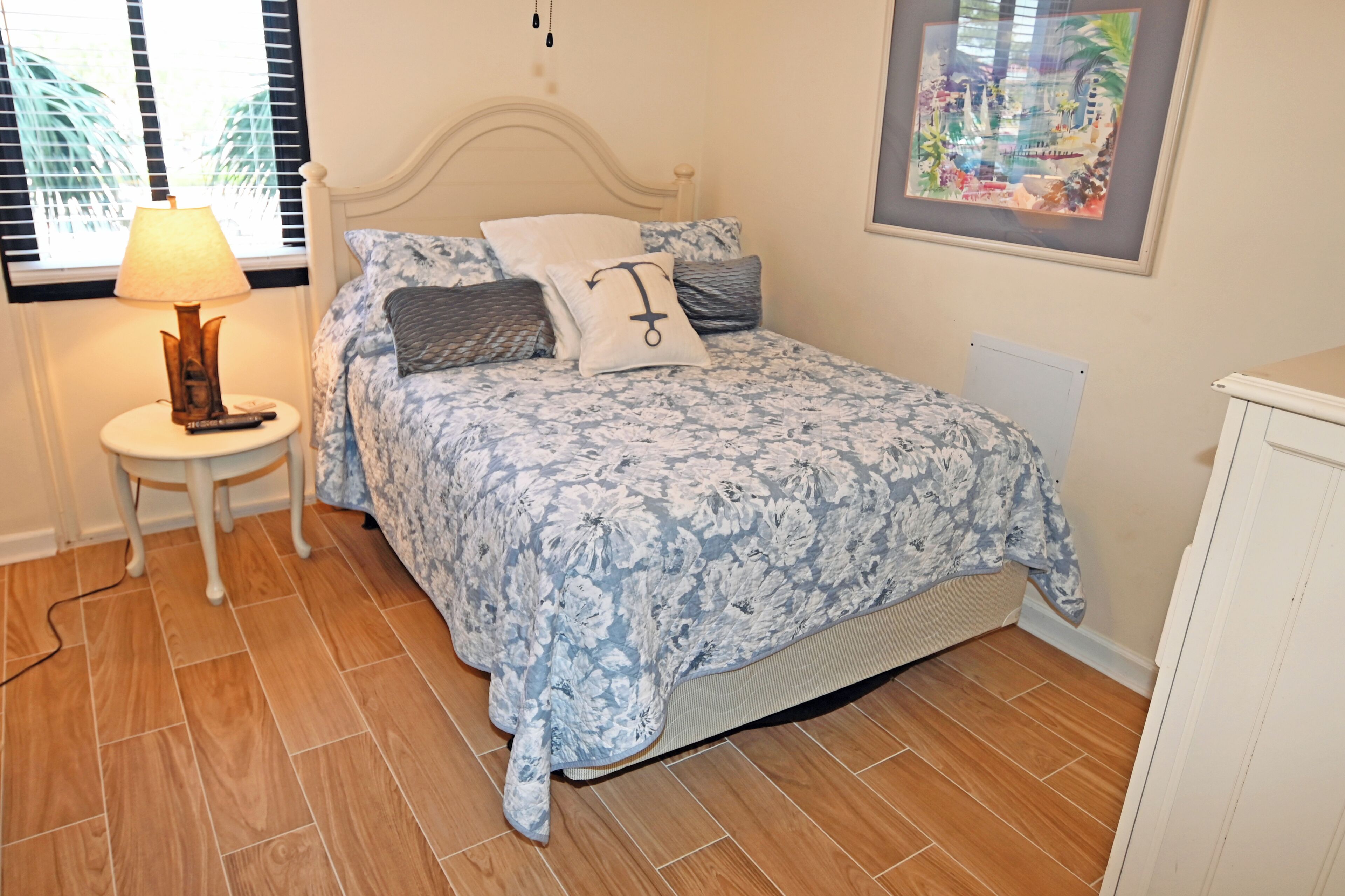 A bedroom with a floral bedspread, a bedside lamp, a framed picture on the wall, and a radiator.
