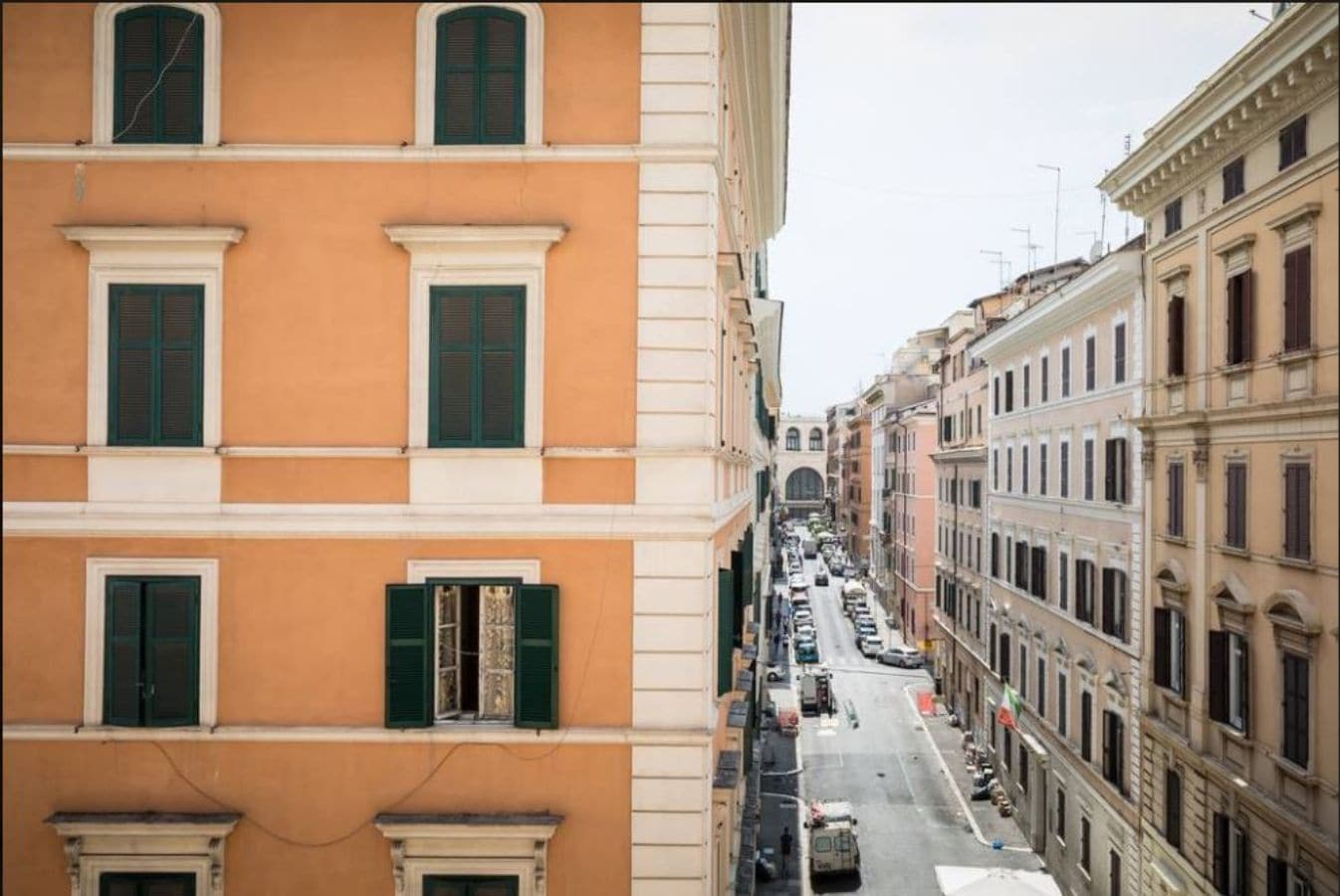 A narrow street lined with multi-story buildings, featuring uniform architectural styles with large windows and shutters.