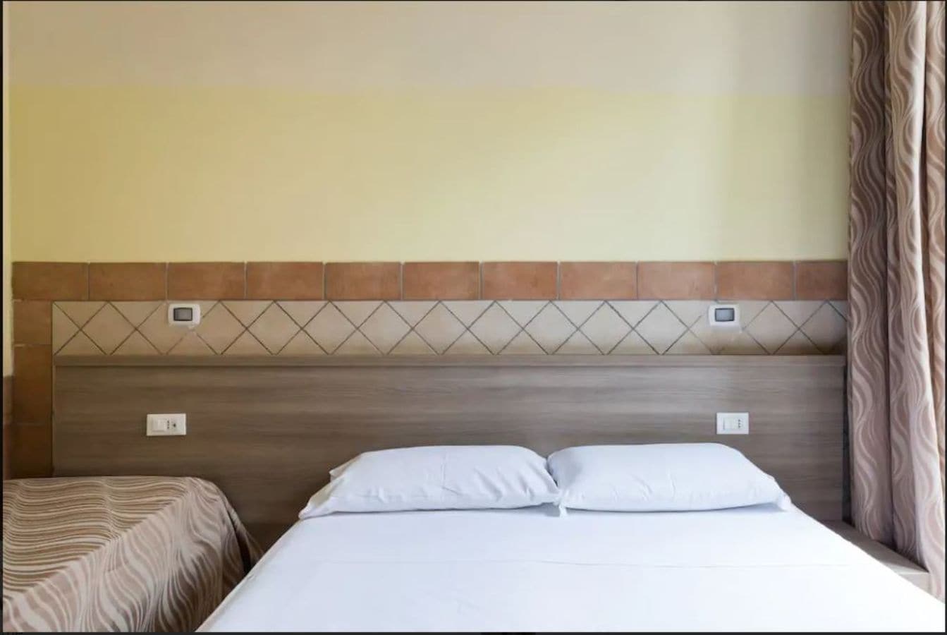 A hotel room with a bed, two bedside tables, and a headboard with a geometric pattern.