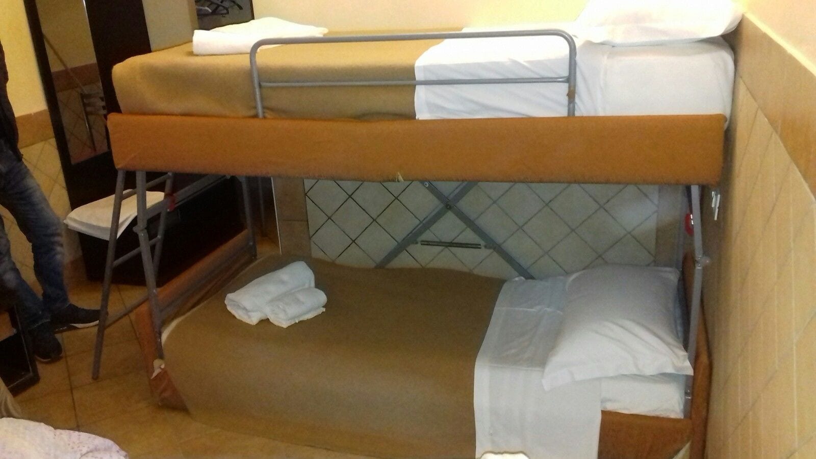 A bunk bed with a mattress and pillows, a chair, and a tiled wall.