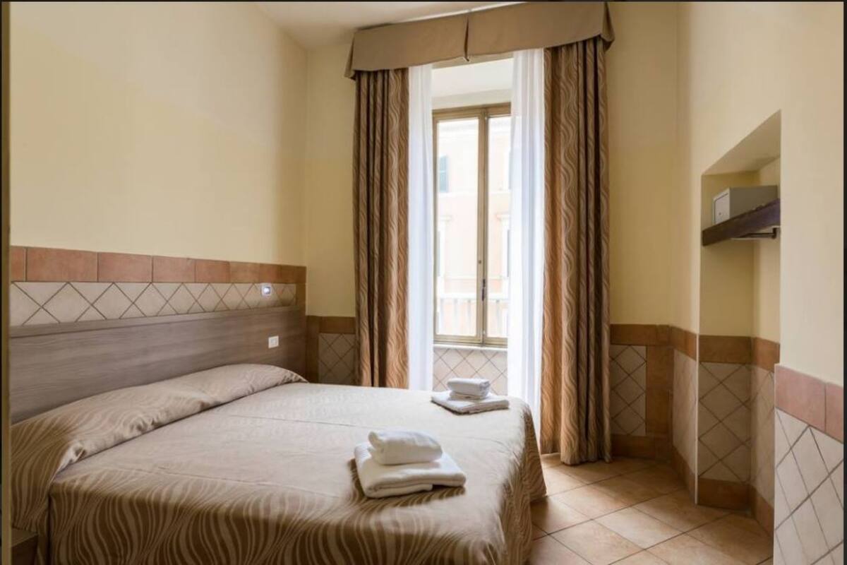 A bedroom with a bed, a window with curtains, and a tiled floor.