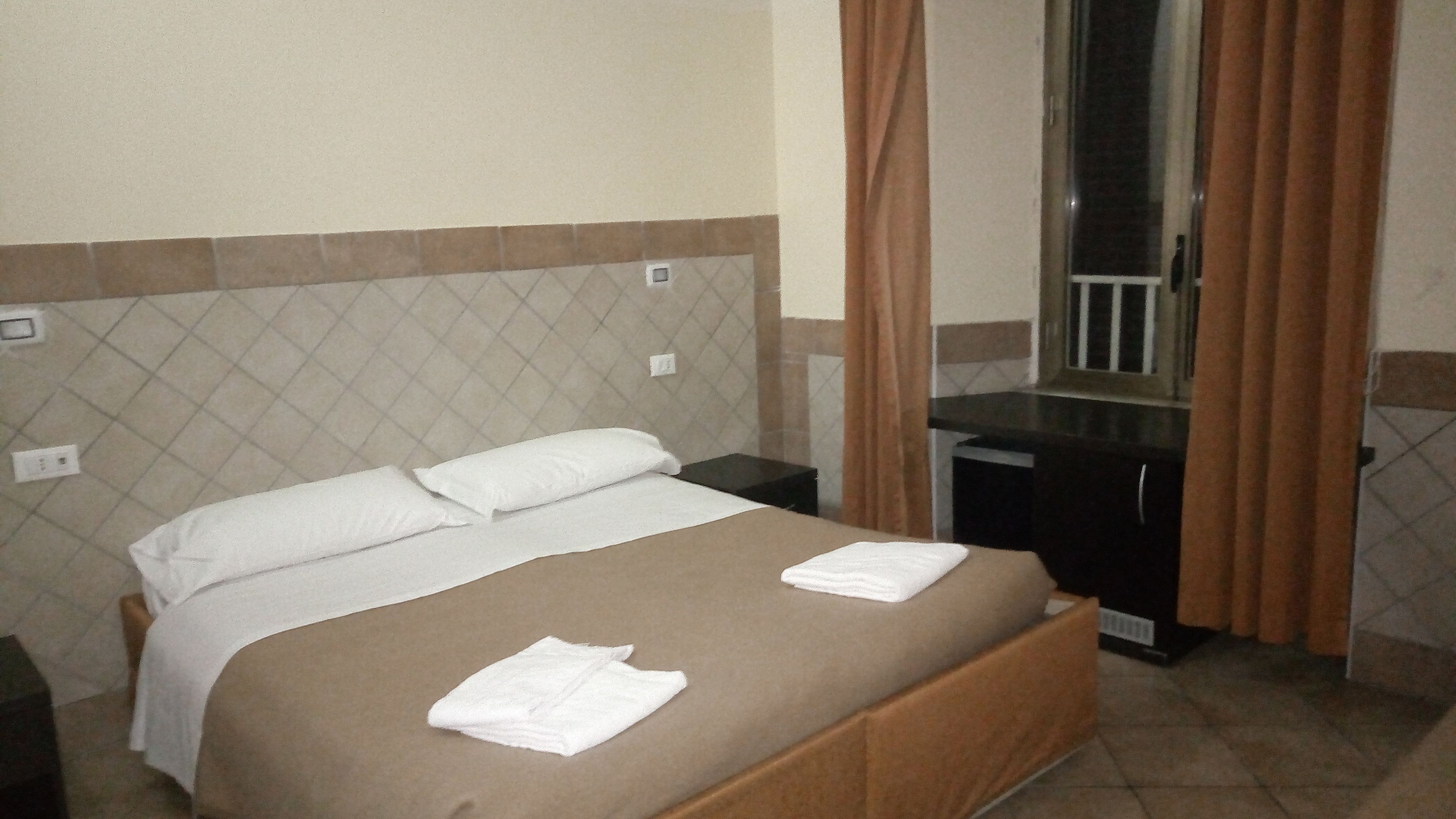 A hotel room with a bed, a nightstand, a mirror, and a window with curtains.