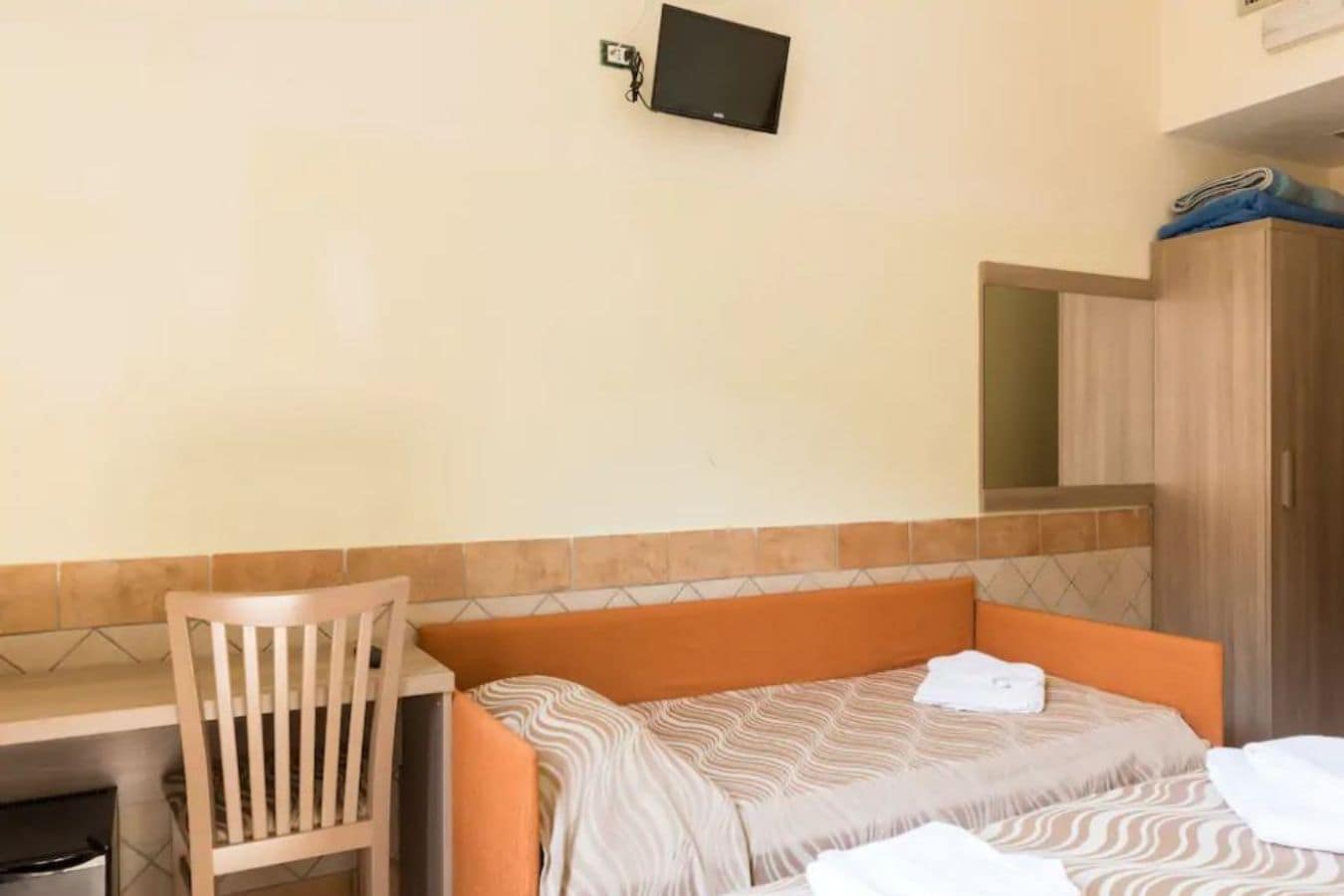 Habitación de hotel con una cama, una silla, un escritorio y un televisor montado en la pared.