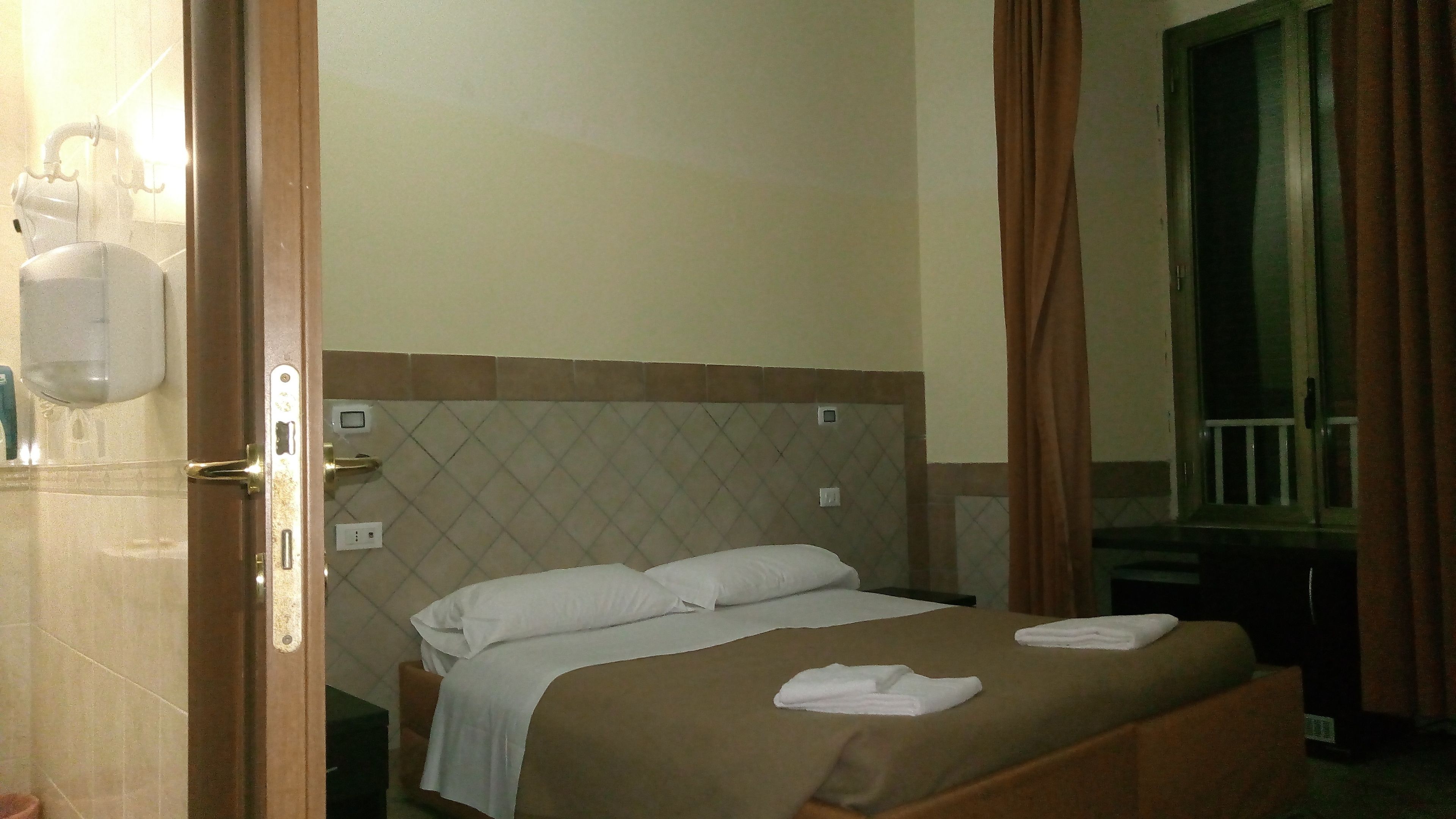 A hotel room with a bed, a nightstand, a mirror, and a window with curtains.