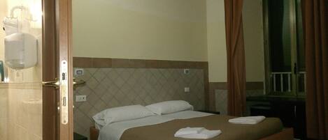 A hotel room with a bed, a nightstand, a mirror, and a window with curtains.