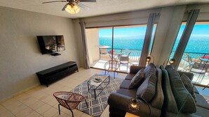 Ein modernes Wohnzimmer mit einer Couch, einem Couchtisch, einem Fernseher und einem Balkon mit Meerblick.