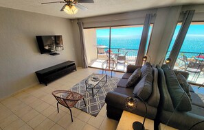 Una sala de estar moderna con sofá, una mesa de centro, televisor y un balcón con vistas al océano.