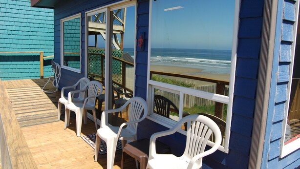 Una terraza con sillas de plástico blanco y una mesa, con vista al océano.