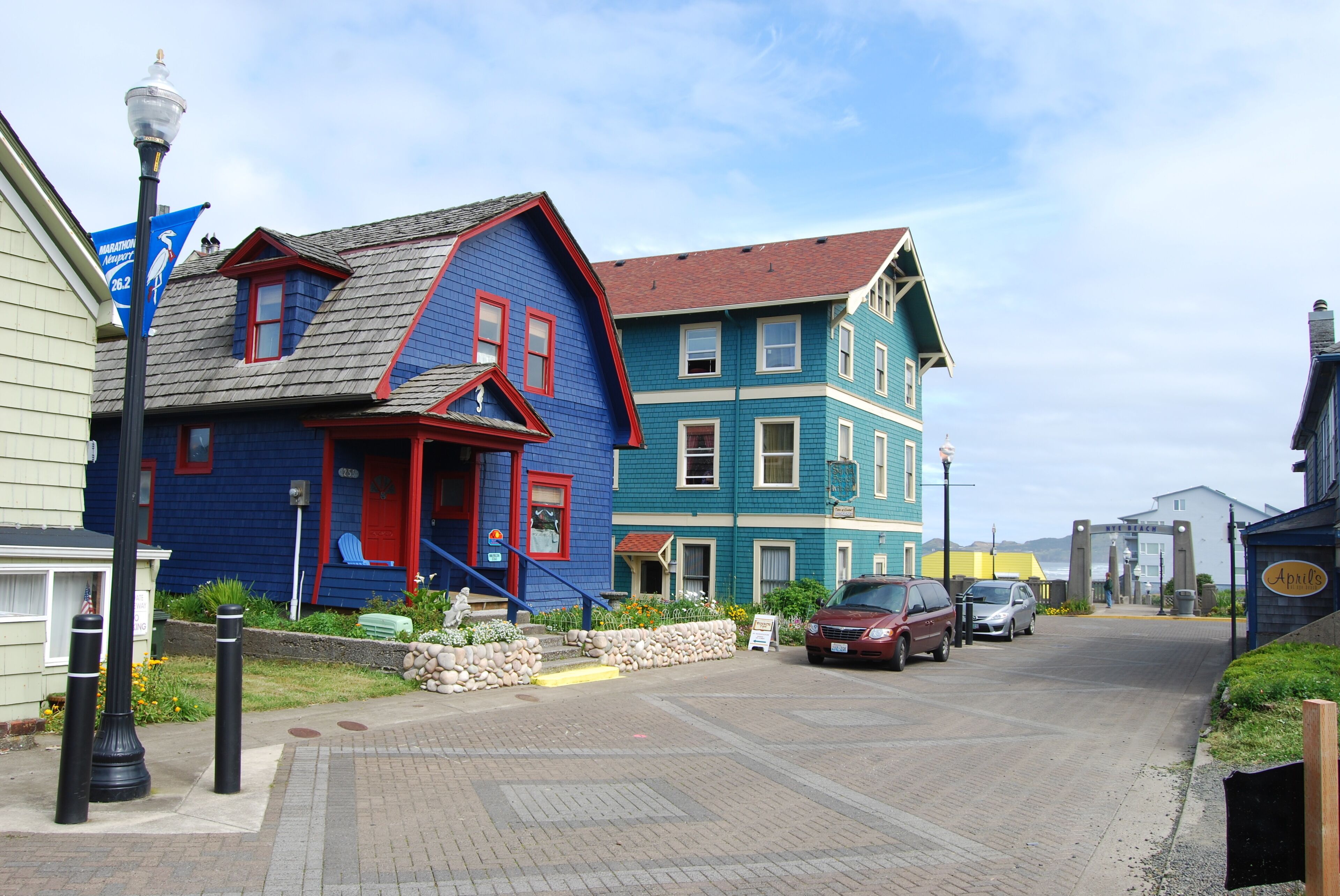 A street view with colorful houses, a paved road, and parked cars.