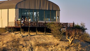 A building with a curved roof, large windows, and a deck area with people. - Ugab Terrace Lodge (Khorixas)