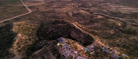 An aerial view of a desert landscape with a small cluster of buildings, a road, and distant mountains.