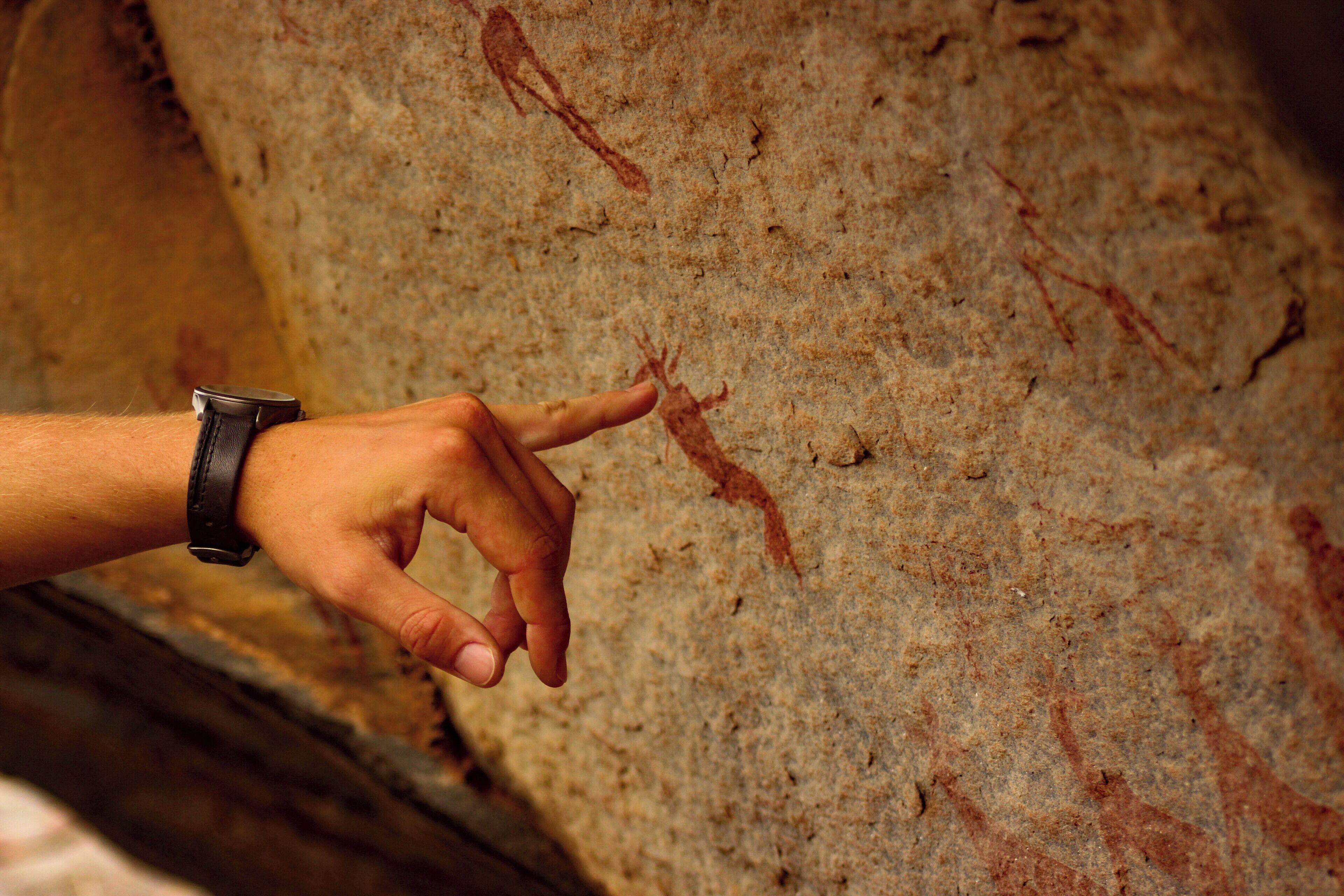A hand pointing at a rock surface with ancient carvings.