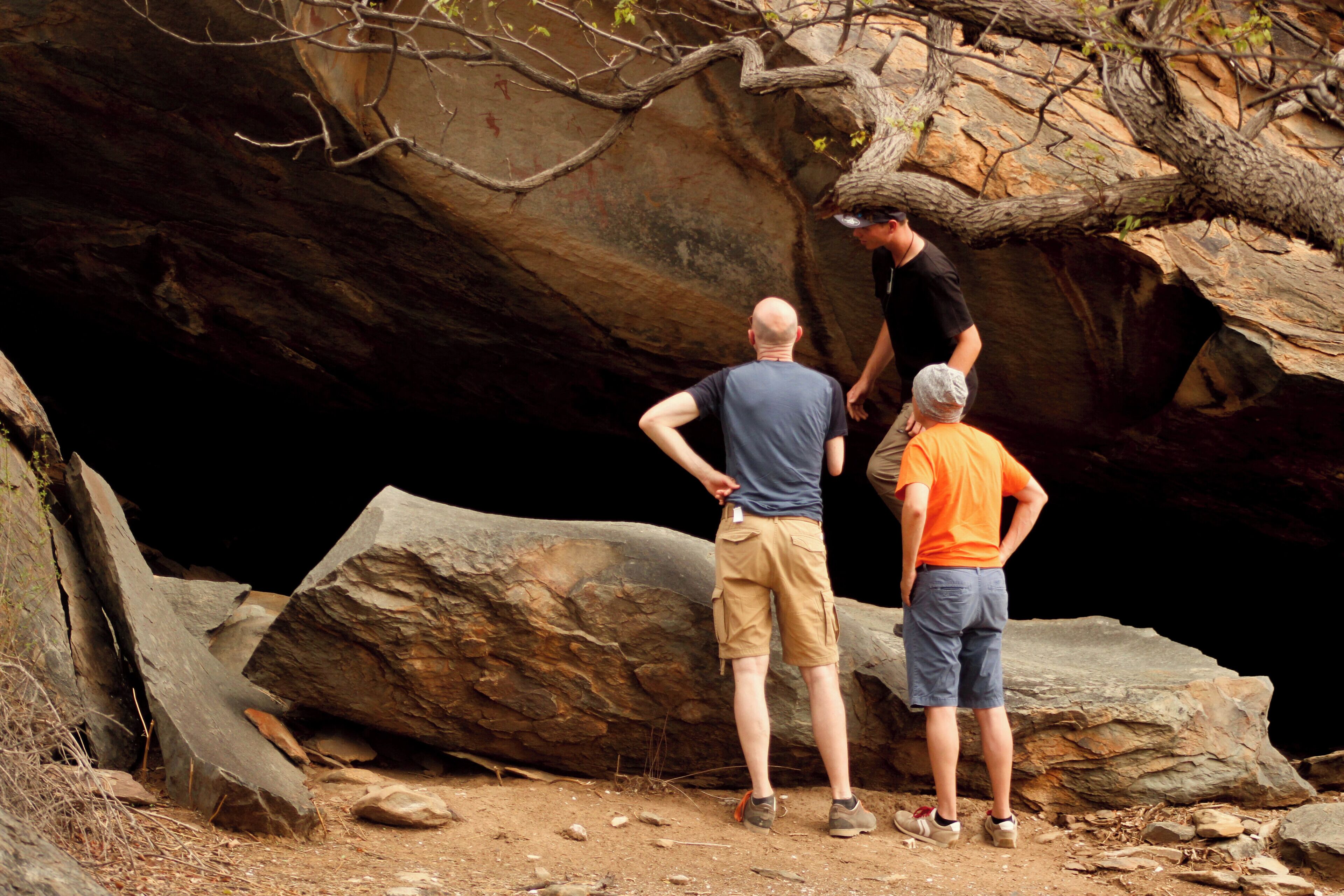 Three people standing near a large rock formation.