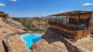 A pool with a stone border, a wooden deck, and a view of the landscape. - Ugab Terrace Lodge (Khorixas)