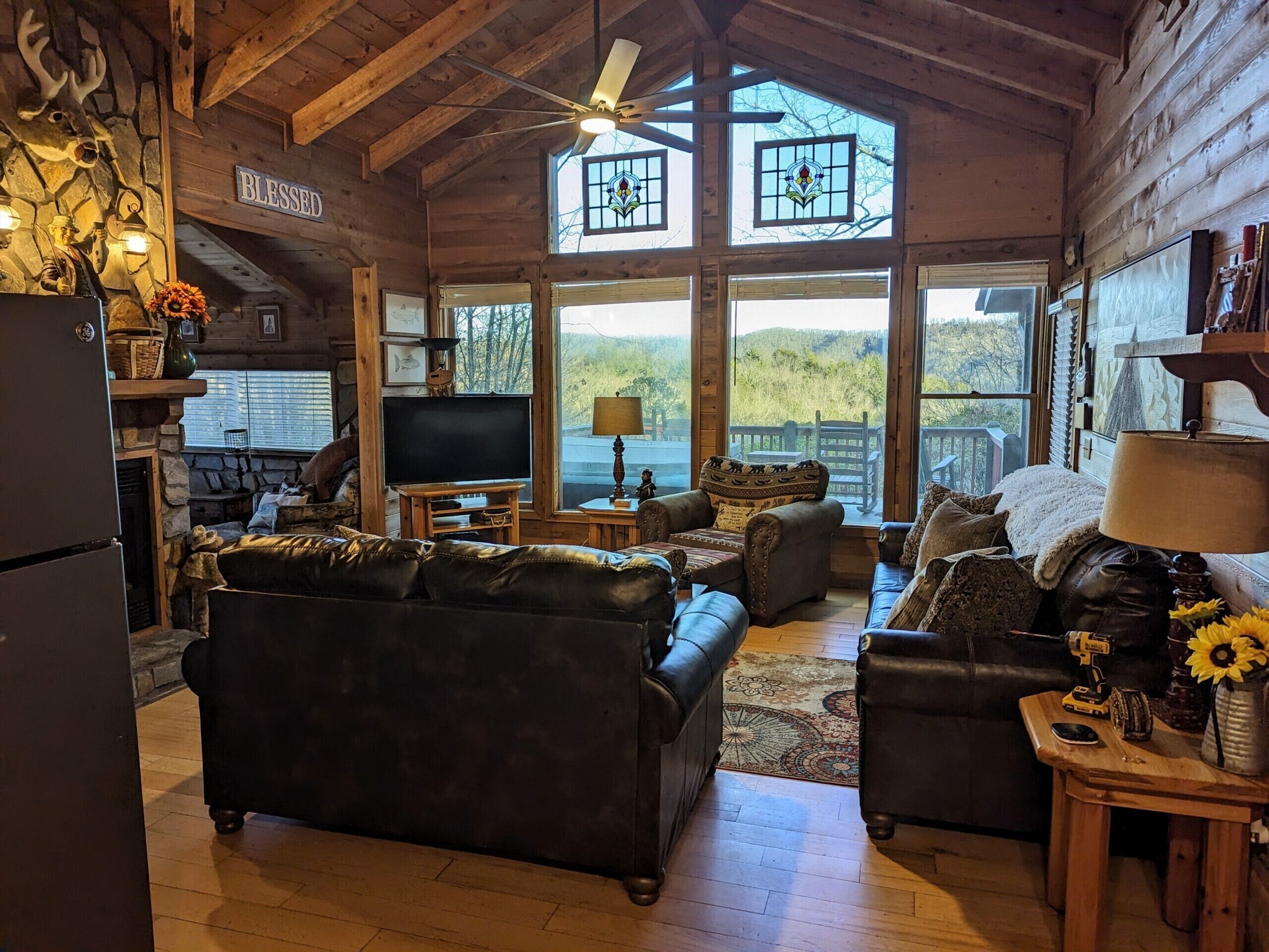 Interior acogedor de una cabaña de troncos con chimenea, televisor y un ventanal grande con vistas a un paisaje pintoresco.