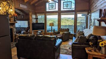 Interior acogedor de una cabaña de troncos con chimenea, televisor y un ventanal grande con vistas a un paisaje pintoresco.