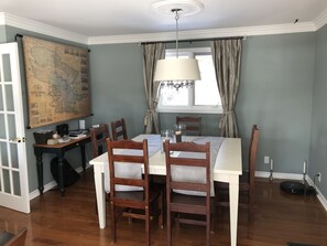 Uma sala de jantar com um mapa na parede, um candelabro e uma mesa de jantar com cadeiras.