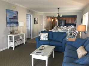 A living room with two blue sofas, a white coffee table, and a dining area with white chairs and a table.