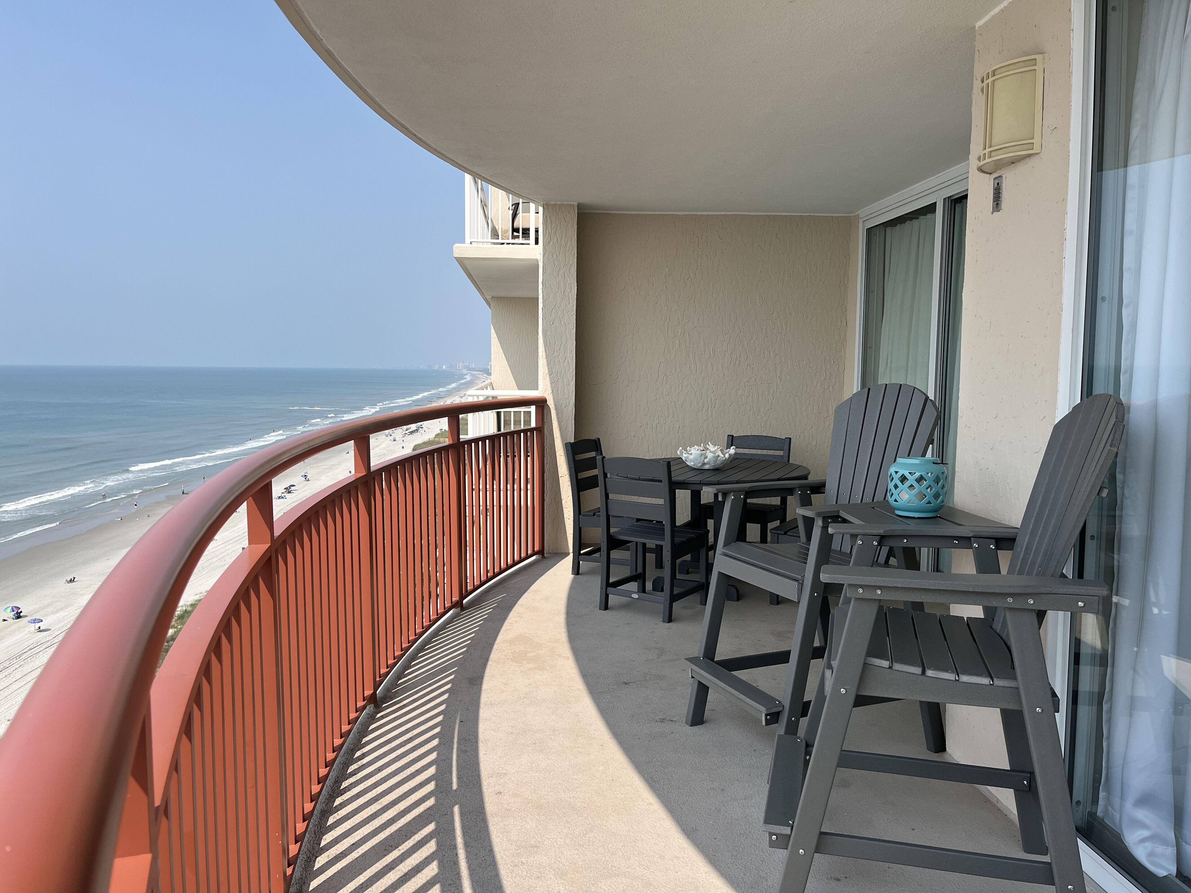 A balcony with a view of the beach, a table with chairs, and a potted plant.