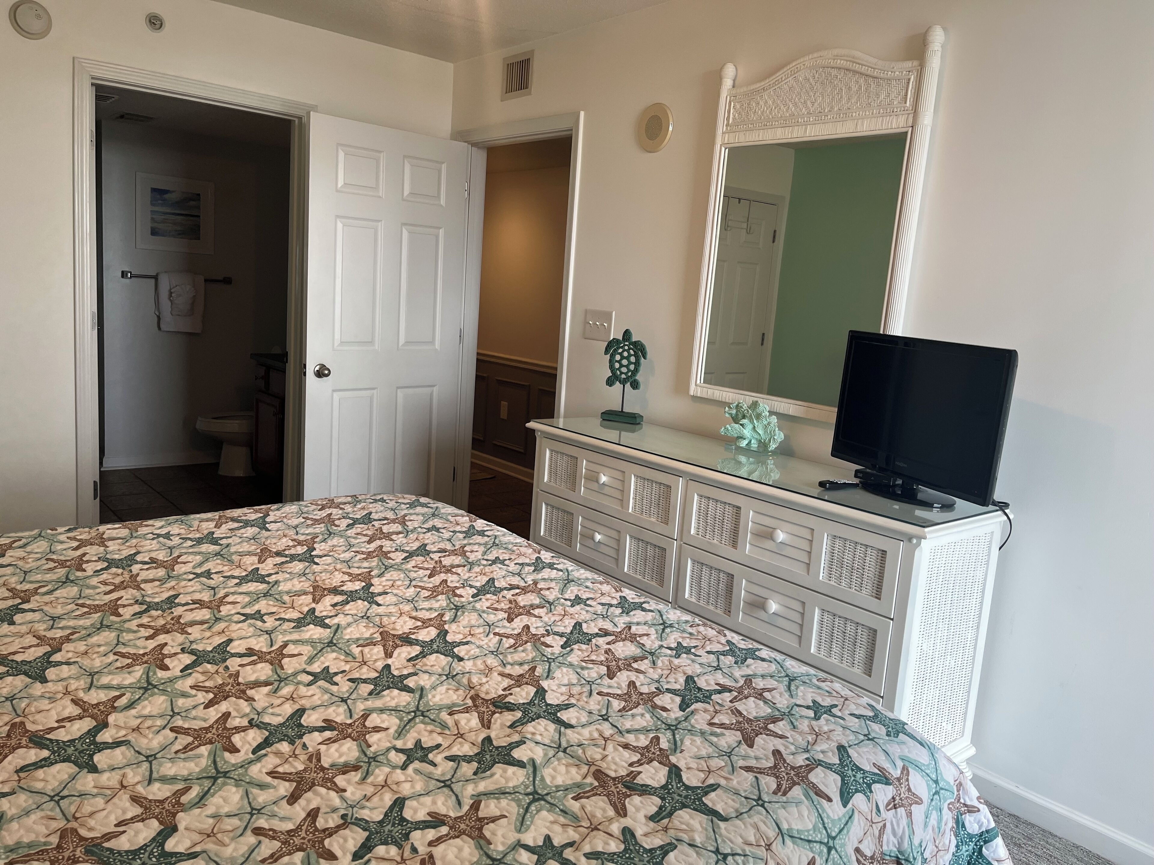 A bedroom with a bed, dresser, television, and a door leading to another room.