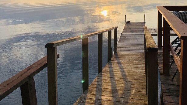 A wooden pier extending into calm water with a sunset in the background.