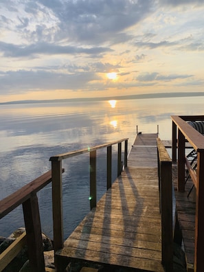Eine Holzstege, der sich in ruhiges Wasser erstreckt, mit einem Sonnenuntergang im Hintergrund.