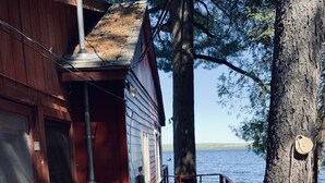 A wooden cabin with a dock extending to a body of water, surrounded by trees.