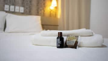 A neatly made bed with white linens, a bottle of lotion, and a towel with 'ELLUS HOTEL' branding.