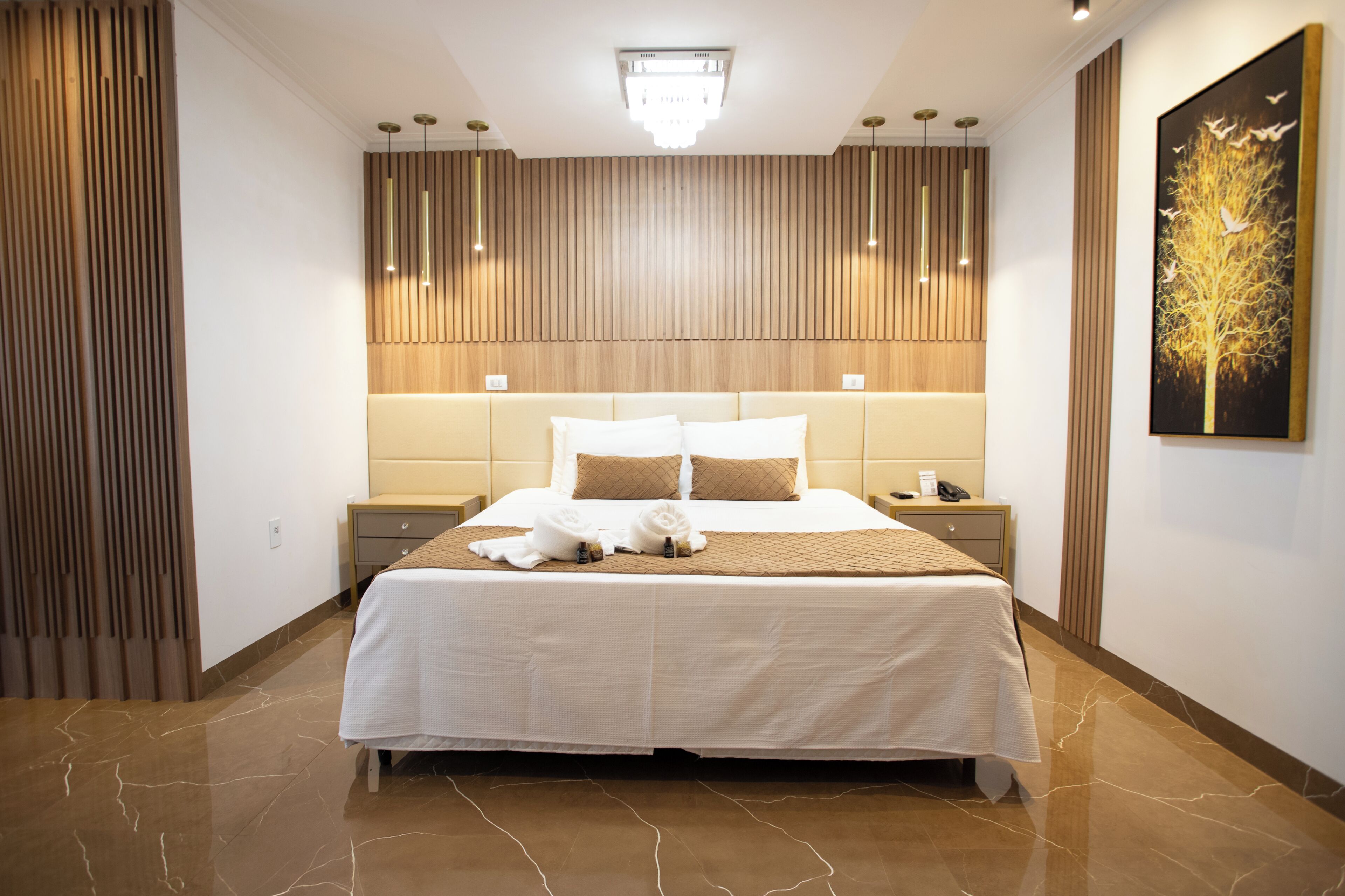 Una habitación de hotel con una cama grande, una mesita de noche, una lámpara de pared y un cuadro.