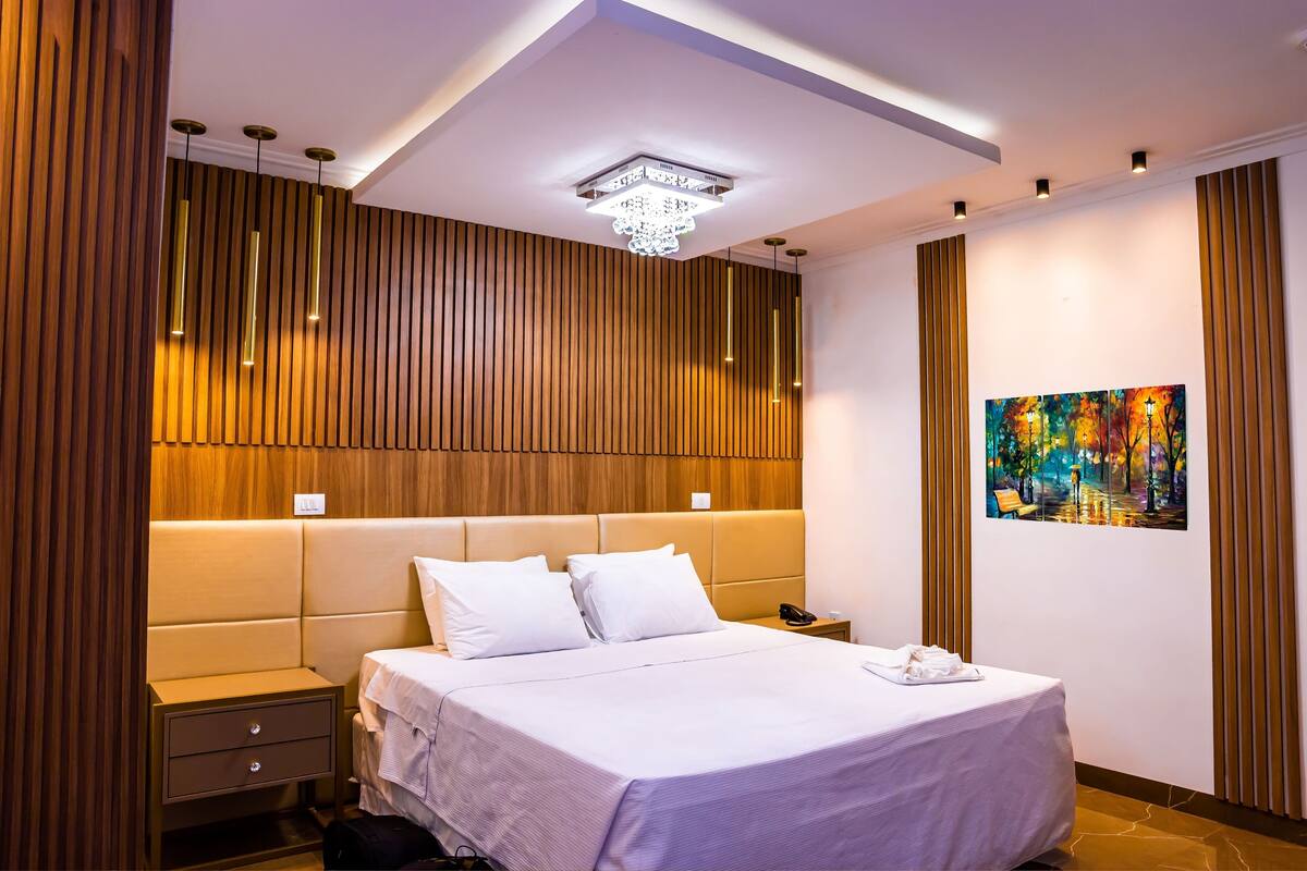 A modern hotel room with a large bed, bedside tables, a nightstand, and a ceiling light fixture.