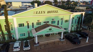 Un hotel con fachada verde, un acceso cubierto y varios coches aparcados.