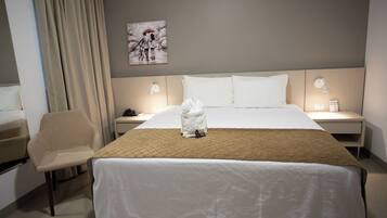 Una habitación de hotel con cama, una silla, una mesita de noche, una lámpara y un cuadro en la pared.