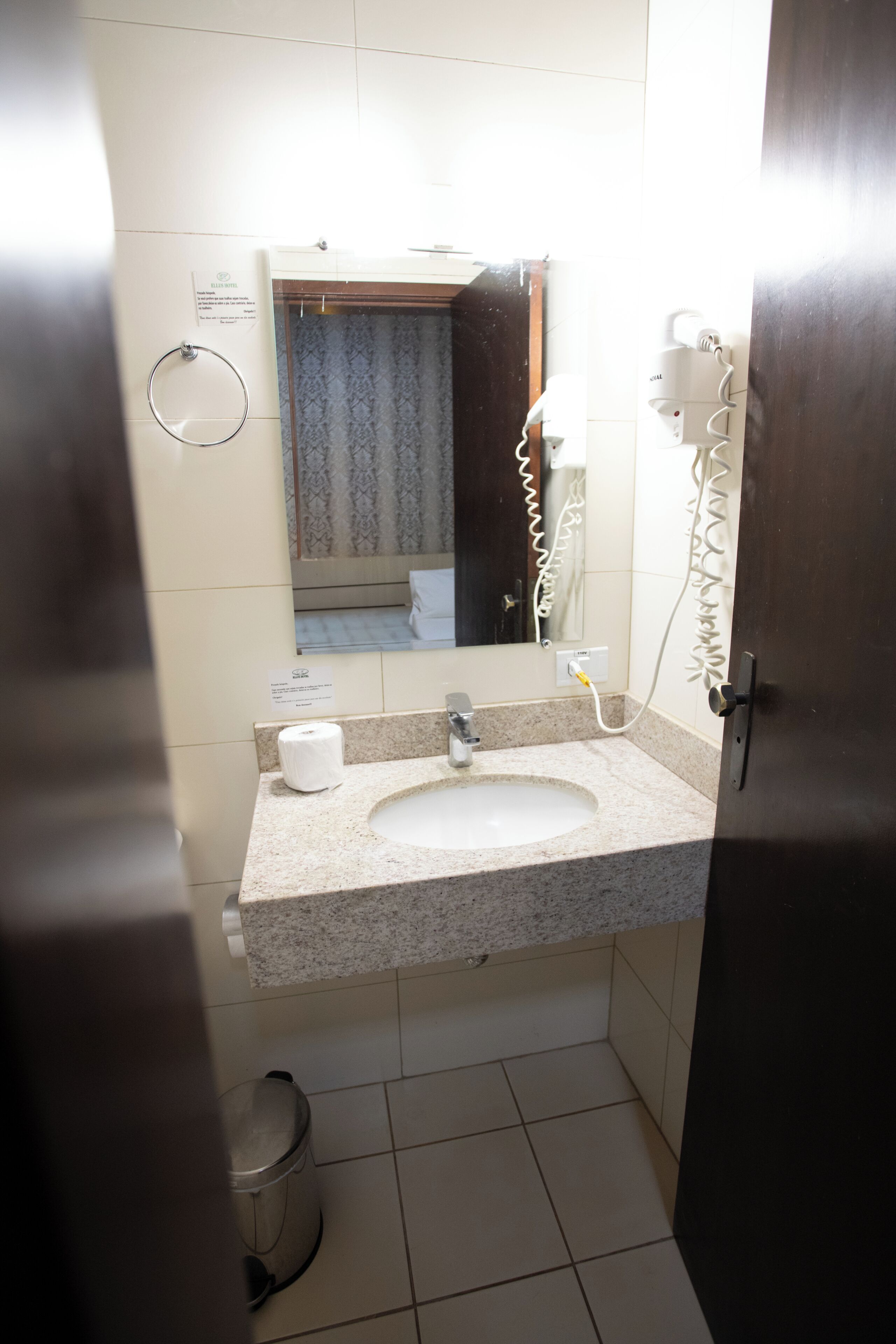 Uma casa de banho com lavatório, espelho, suporte para toalhas e secador de cabelo na parede.
