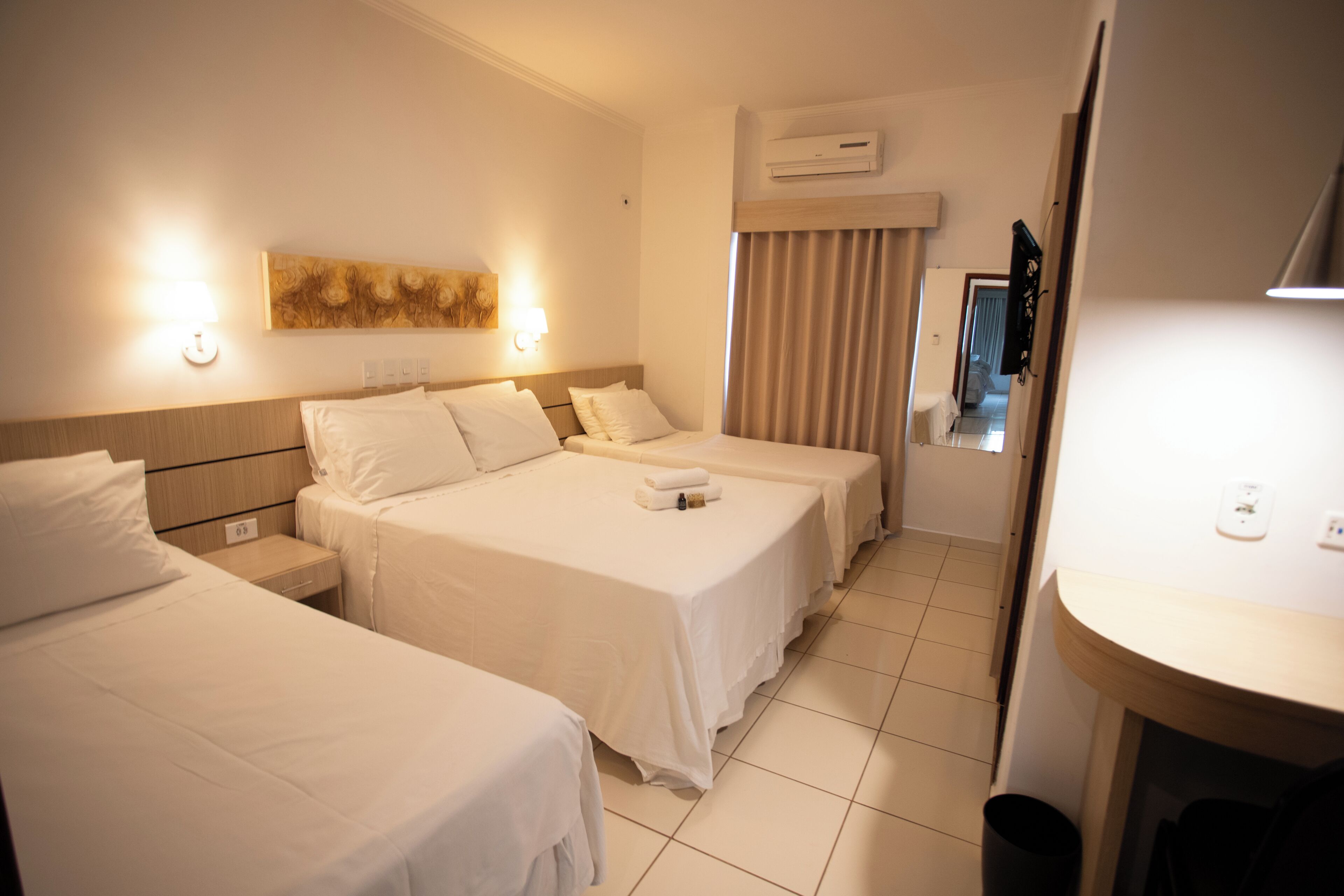 A hotel room with two beds, a nightstand, a wall-mounted air conditioner, and a bathroom visible through a door.