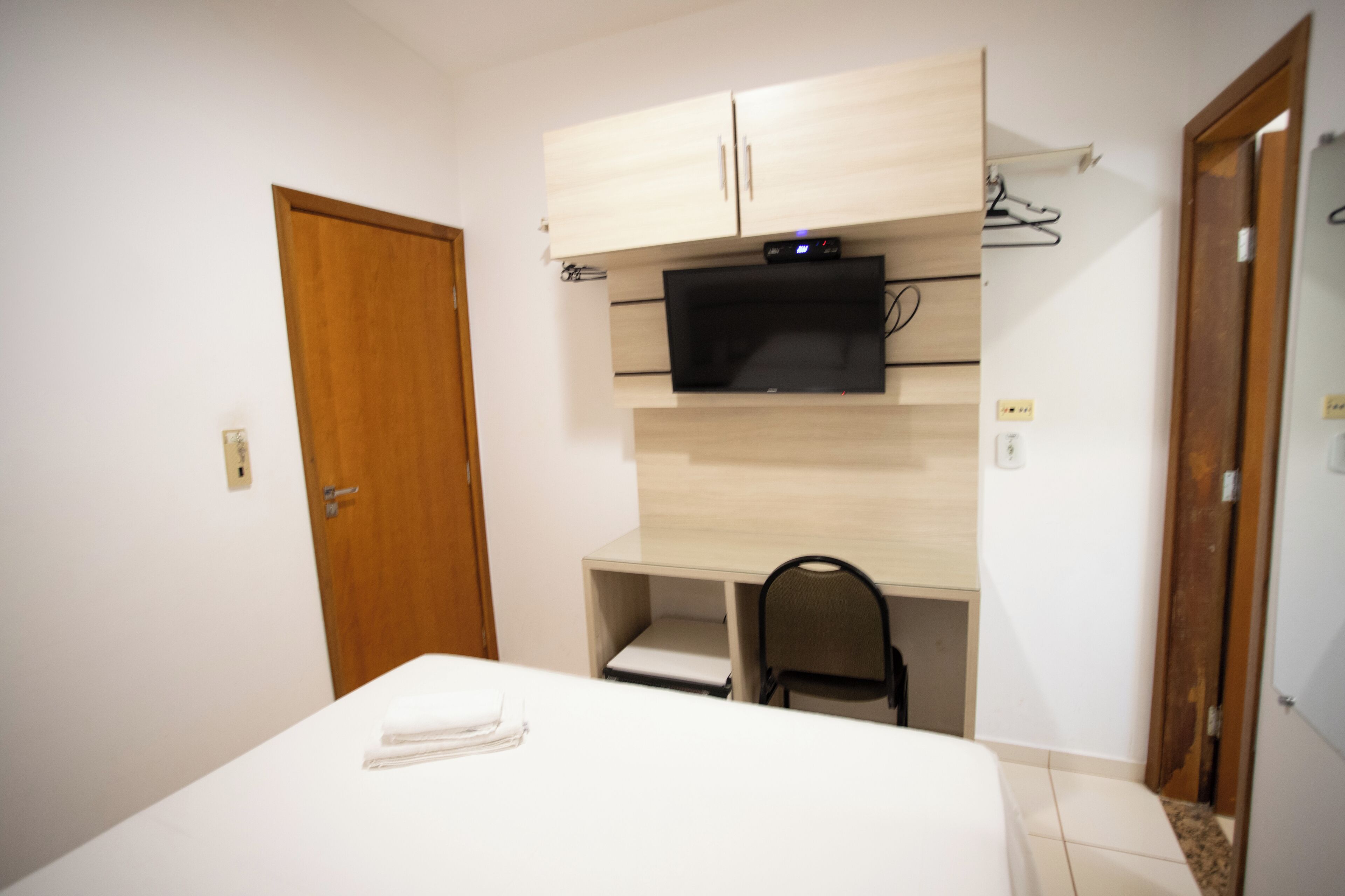 A bedroom with a bed, a desk with a chair, a television, and a wardrobe.