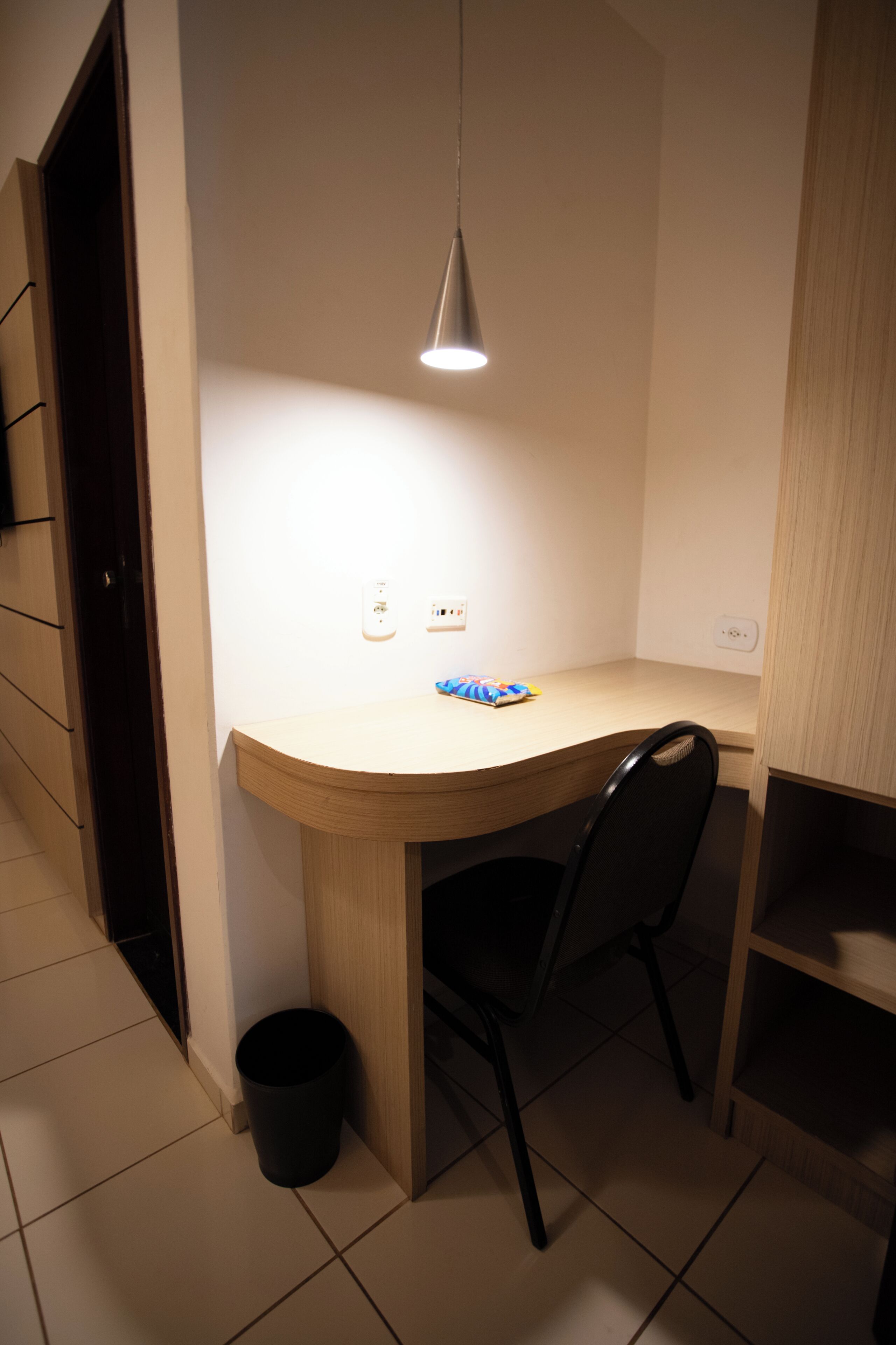 A compact room with a desk, chair, and a hanging light fixture.