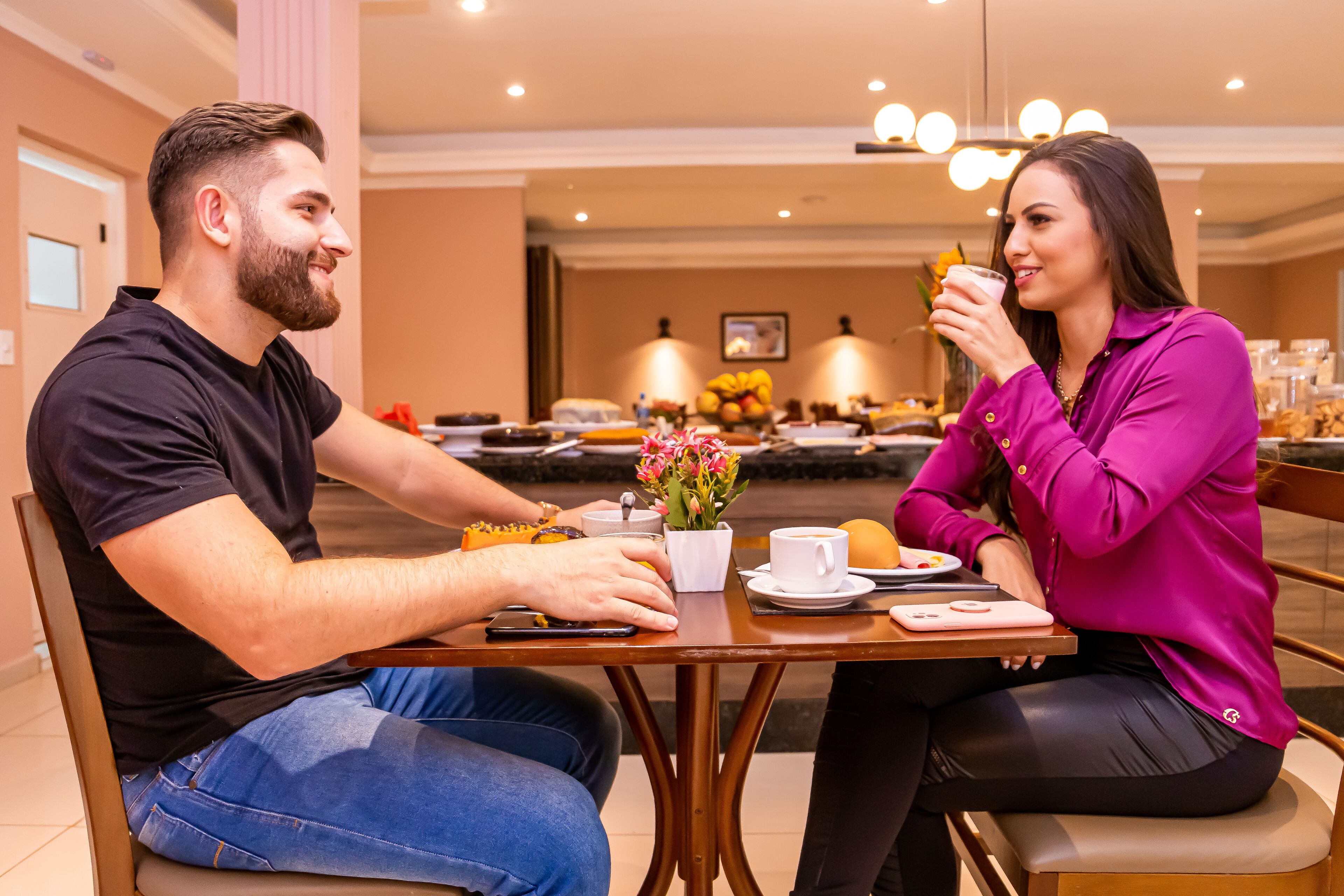 Un comedor con una mesa dispuesta para dos personas, que incluye una taza de café, un plato con comida y un pequeño jarrón con flores.